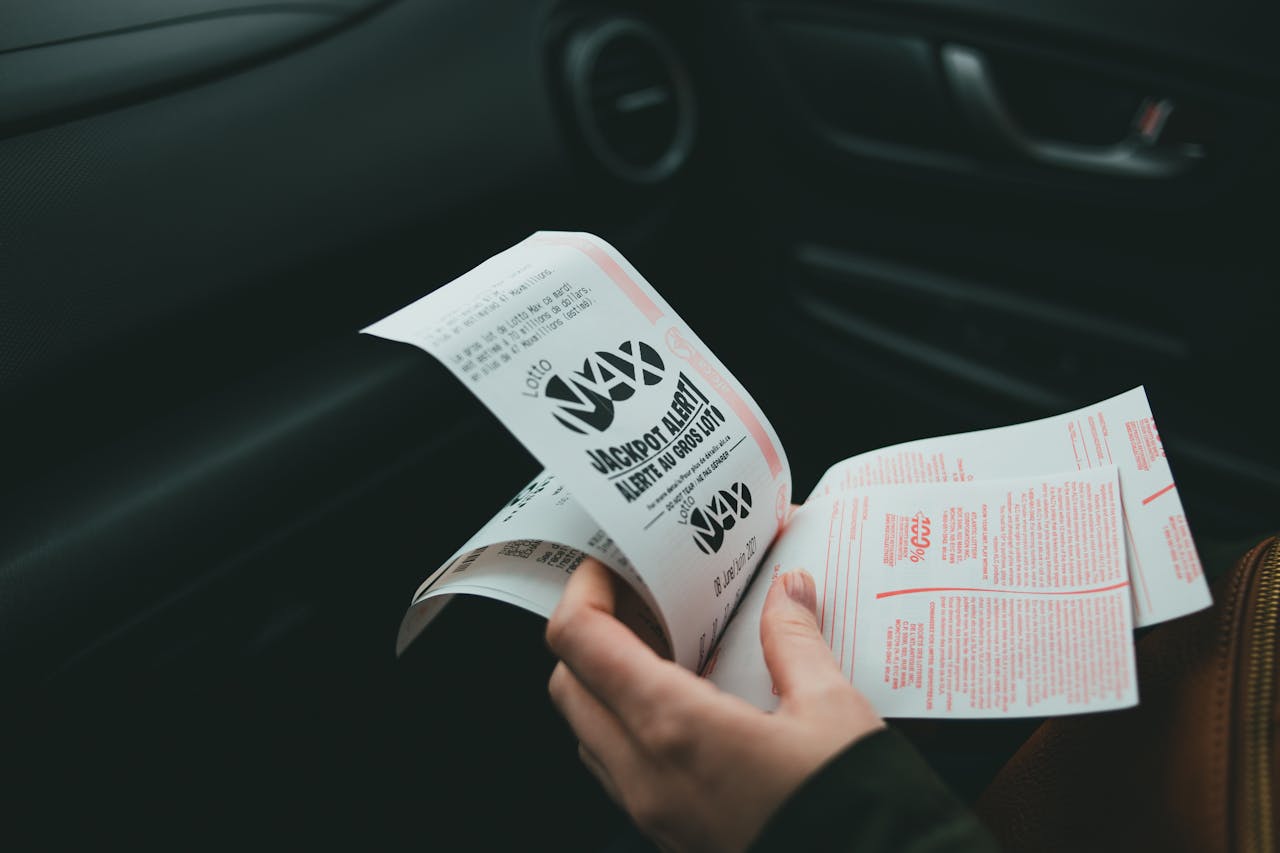 expertise-01 Close-up of hands holding Lotto Max papers inside a car, symbolizing luck and chance.